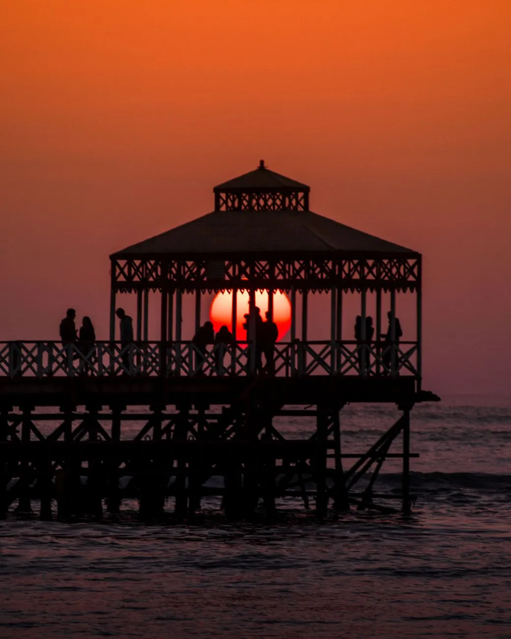 The sun sets through the pier pavilion at Huanchaco